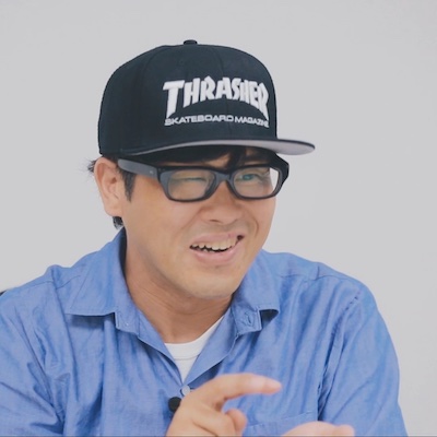 高根澤史生のプロフィール写真。THRASHERのキャップ、黒縁メガネ、青いシャツ